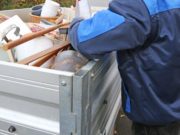 Eine Person die an einem Truck steht, in dem viel Müll, Möbel und sonstige Sachen drin sind.