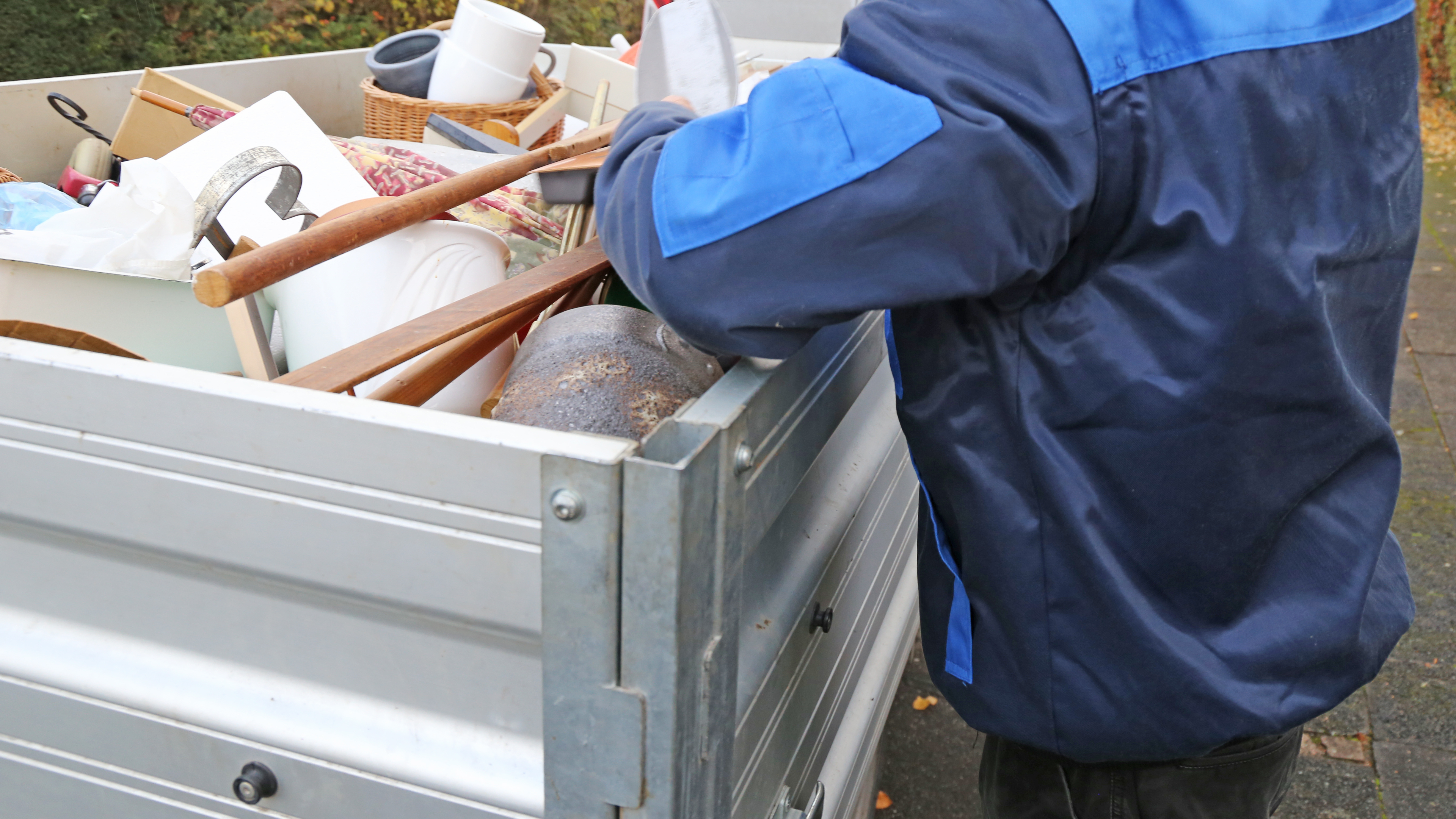 Eine Person die an einem Truck steht, in dem viel Müll, Möbel und sonstige Sachen drin sind.